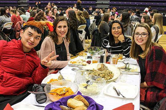 Photo of international students at a 2024欧洲杯官方投注 harvest dinner, smiling for the camera as they eat dinner