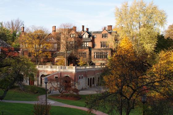 A red-bricked Mellon Hall on Chatham University's Shadyside campus sits on a green campus surrounded by colorful autumn leaves. 